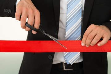 Businessman Cutting Red Ribbon With Scissors