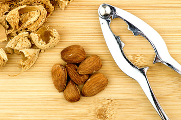 Almonds, shells with metal nut cracker on wooden background
