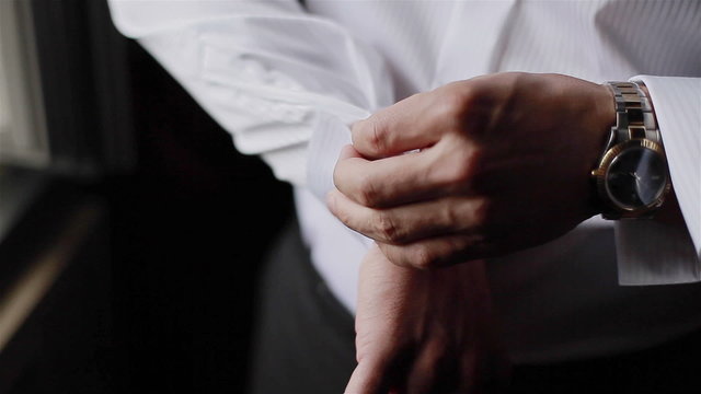 Man puts cufflinks on sleeves of white shirt. Close-up