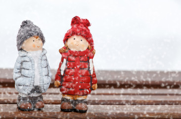 two dolls stand on desk at winter day, snowing