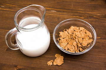 Bowl with cereal and jug of milk on wooden table