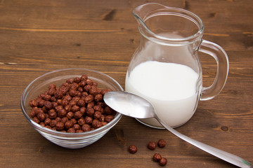 Bowl with chocolate cereals and jug of milk on wooden table