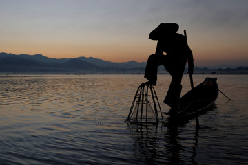En silhouette, un pêcheur plonge son filet dans le lac