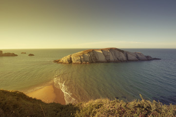 Little stone island in the ocean seen from the cliffs at sunset