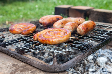 Tasty sausages cooking over the hot coals on a barbecue fire out