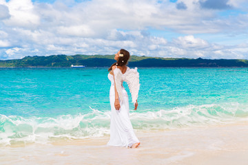 Fototapeta na wymiar Beautiful young bride with angel wings on the sea coast. Tropica