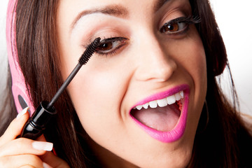 Woman Putting on mascara while listening to Headphones