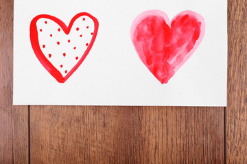 Painted hearts on sheet of paper on wooden table background