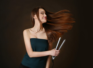 Beautiful young woman with long hair using hair straighteners