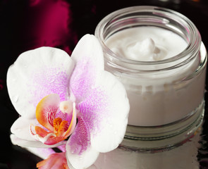 Face cream with orchid flowers on dark background
