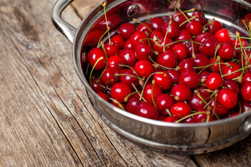 Sweet cherries in colander on color wooden background
