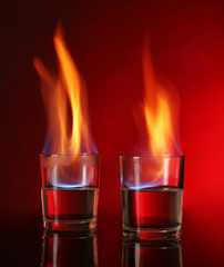 Glasses with burning alcohol on red background