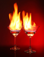 Glasses with burning alcohol on red background