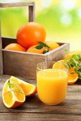 Glass of orange juice with crate of oranges and slices