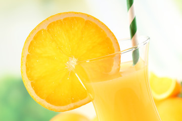 Glass of orange juice with straw and slices on bright