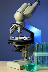 Microscope and test tubes on table, on color background