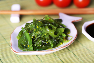 Seaweed salad in plate on bamboo mat background