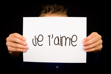 Child holding sign with French word Je T aime - I Love You