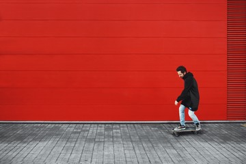 Guy rides his skate in front of red wall