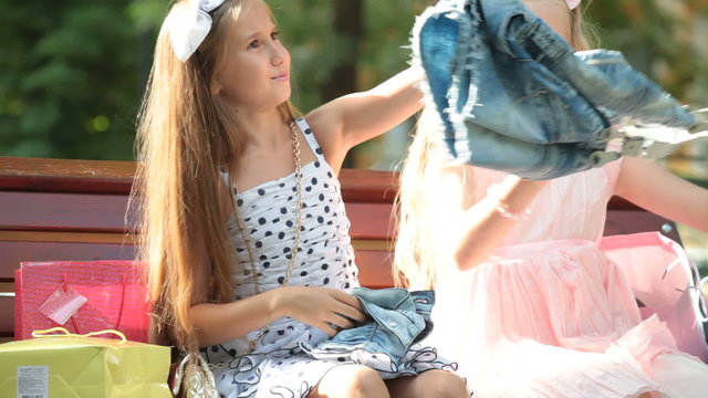 Fashion little girls in summer dresses having fun on a bench