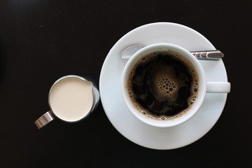 Hot coffee with milk-jug on black background