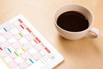 Tablet pc showing calendar on screen with a cup of coffee on a d