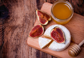 Camembert cheese with honey and figs on a wooden board.