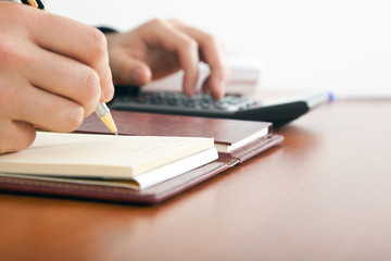 Businessman using a calculator on a wooden desk.