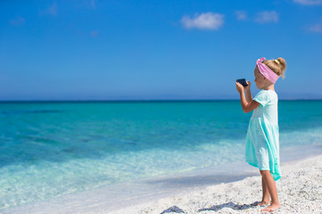 Little cute girl taking pictures on phone at tropical beach