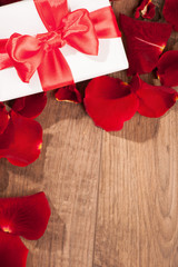 Present box in rose petals on wooden background