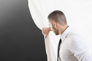 businessman looks behind the curtain a gray blank wall