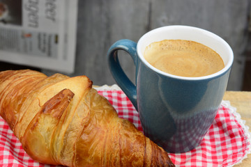 Coffee with croissant on old wooden table and newspaper