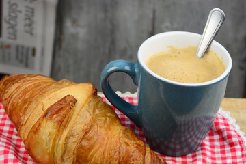 Coffee with croissant on old wooden table and newspaper