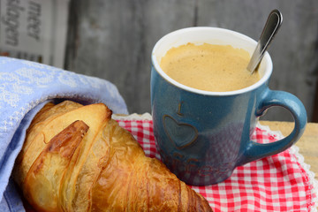Coffee with croissant on old wooden table and newspaper