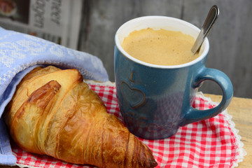 Coffee with croissant on old wooden table and newspaper