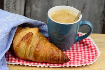 Coffee with croissant on old wooden table and newspaper
