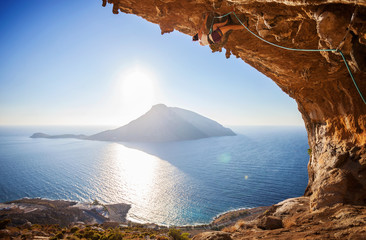 Female rock climber climbing along roof in cave