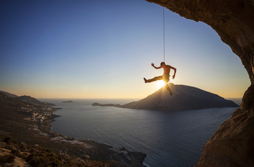 Rock climber hanging on rope while lead climbing at sunset