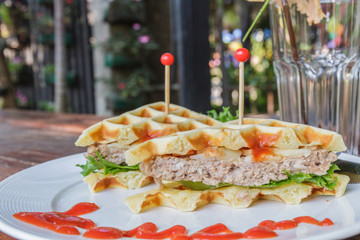 Hamburger made with waffles and pork on white plate.