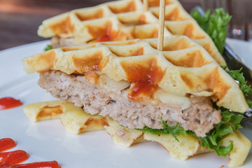 Hamburger made with waffles and pork on white plate.