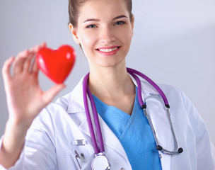 Young woman doctor holding a red heart, standing on gray