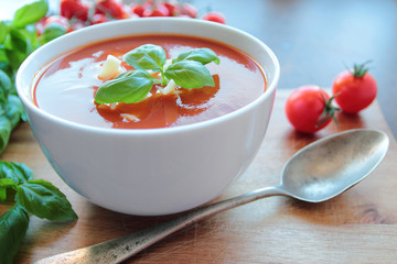 Tasty tomato soup in white bowl with basil leafs