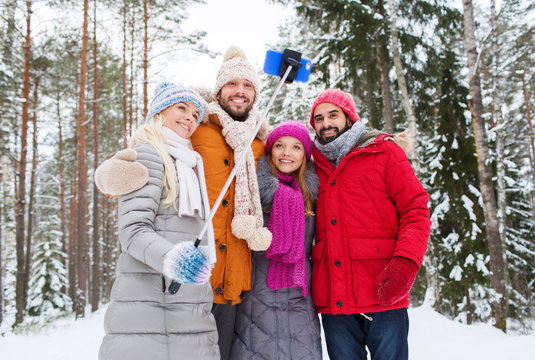 smiling friends with smartphone in winter forest