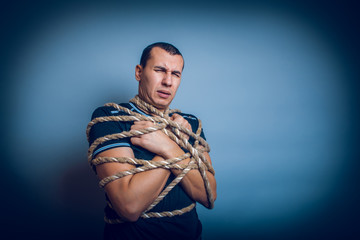 Fototapeta na wymiar male of European appearance brunet tied with rope on a gray back
