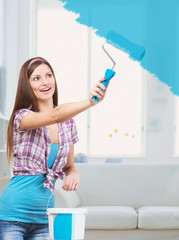 Girl painting walls in her apartment with blue color paint