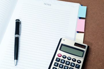 Blank notebook page with black ball pen and calculator on top