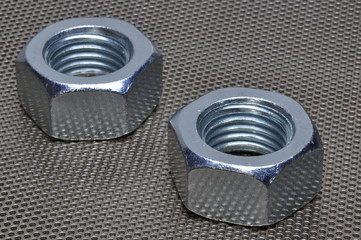Two steel nuts on metal surface with holes