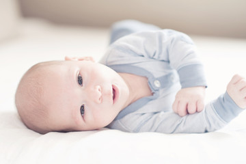 Pretty baby boy in blue rolling on a bed