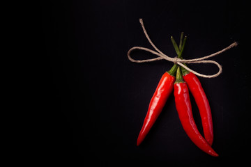 Three hot red chili pepper related by twine with on a black back