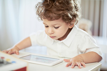 Cute boy in white t-shirt, watching fairy tale on tablet